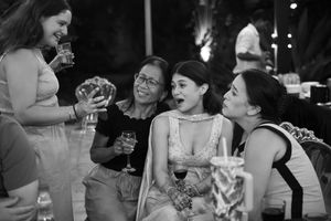 (B&W) One woman shows three other women something on her phone, eliciting one smile and two "awww" faces.