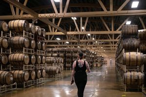 A woman walks down a wide and long brewery space lined by stacks and rows of kegs. The stack 4 high.