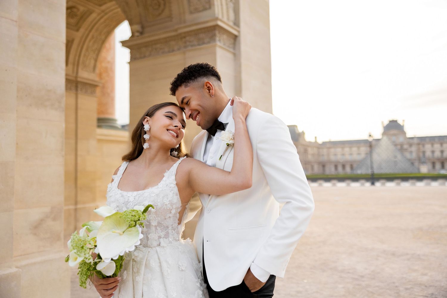 Elegant wedding couple embraces under ornate stone archways during golden hour celebration.