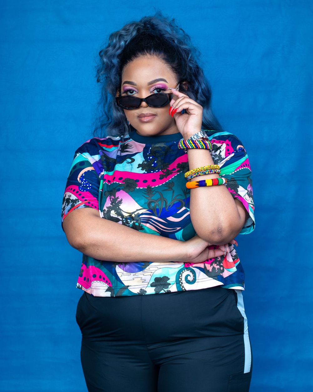 Stylish portrait in colorful print top and sunglasses against bright blue backdrop.