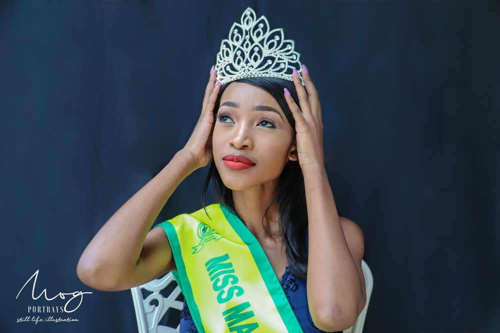 Beauty pageant winner adjusting crystal crown while wearing yellow-green sash.