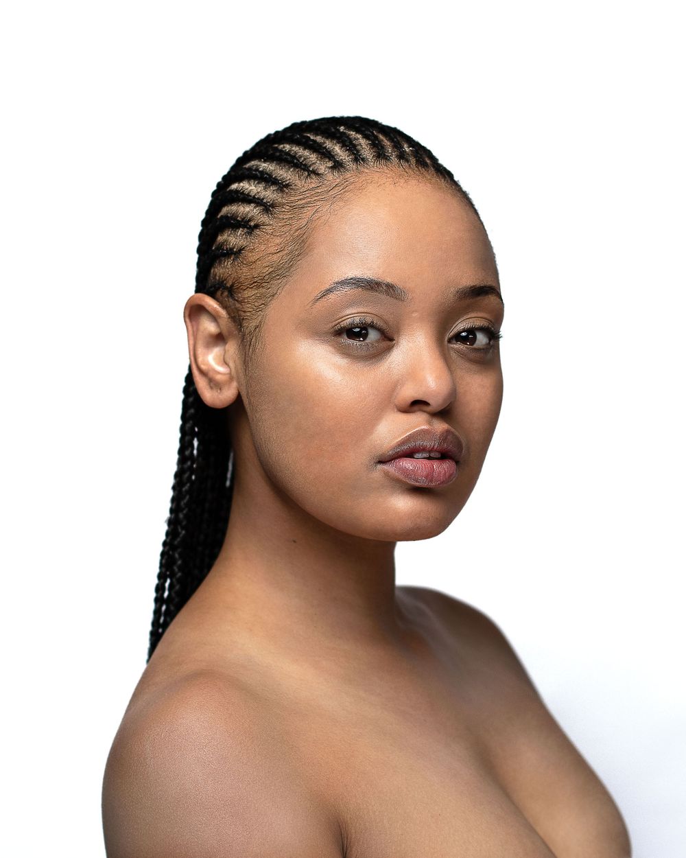 Portrait featuring cornrow braided hairstyle and natural makeup against white background.
