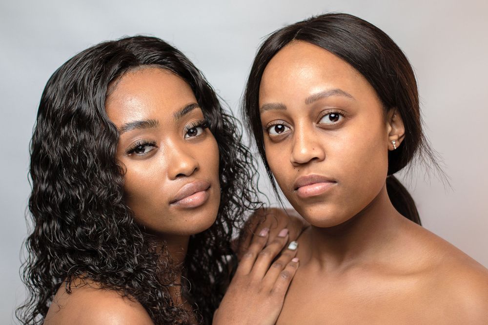Studio portrait of two women with contrasting hairstyles against light background.