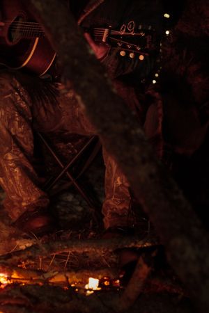 A dark atmospheric shot of a guitar headstock and strings illuminated by dim reddish lighting at night.