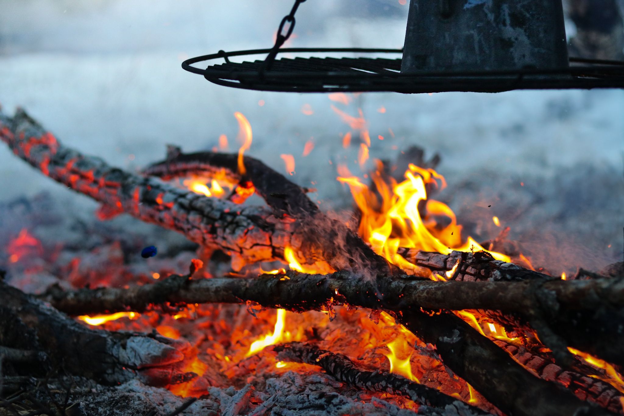 Bright orange flames dance over burning logs in a campfire against a dark background.