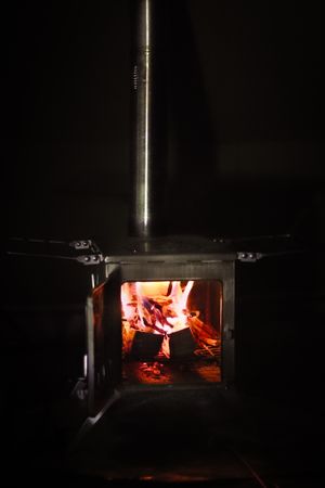 Wood burning stove with glowing flames visible through the open door in dark setting.