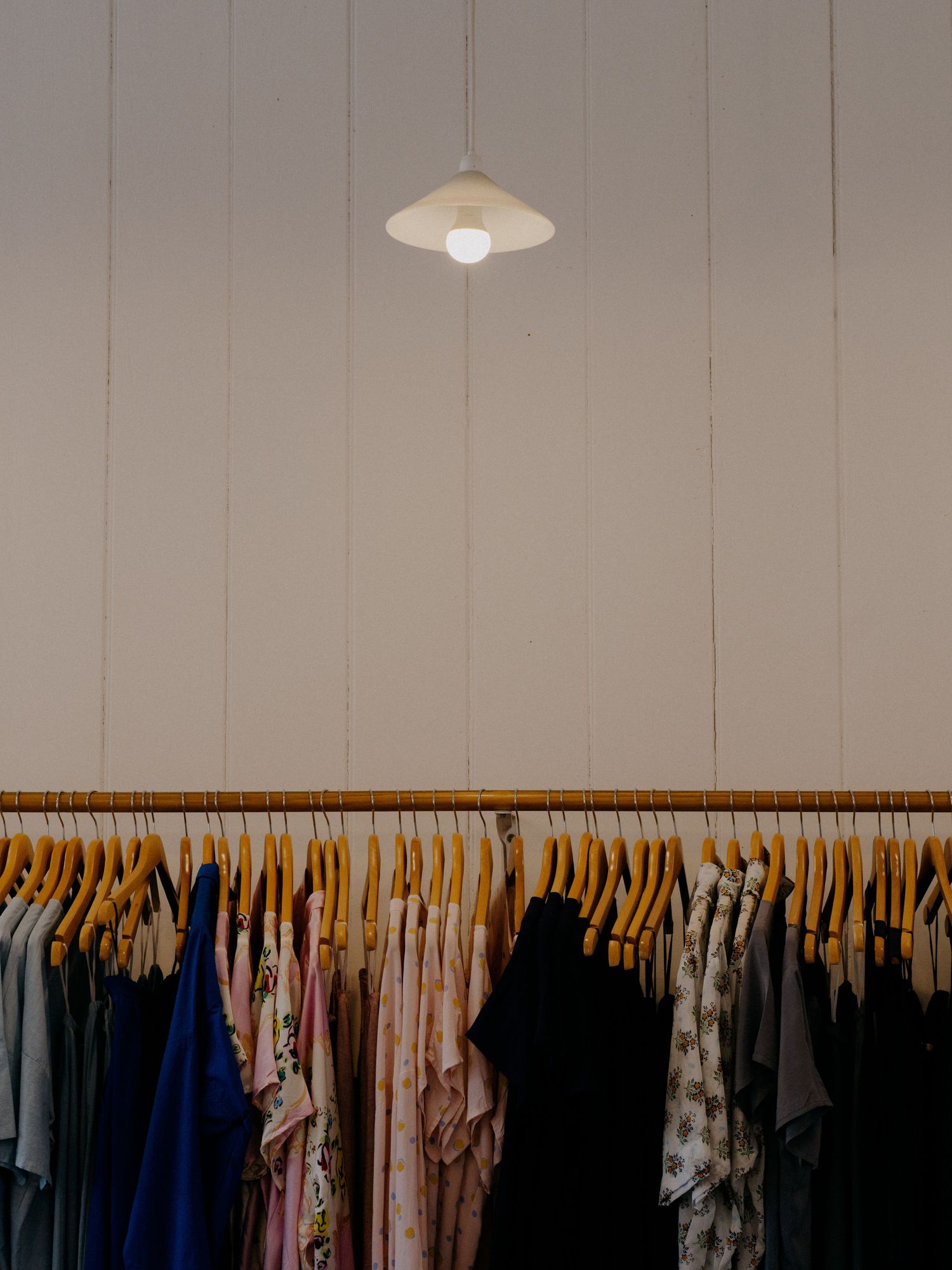 Clothing rack with hangers under a pendant lamp in a minimalist retail space.