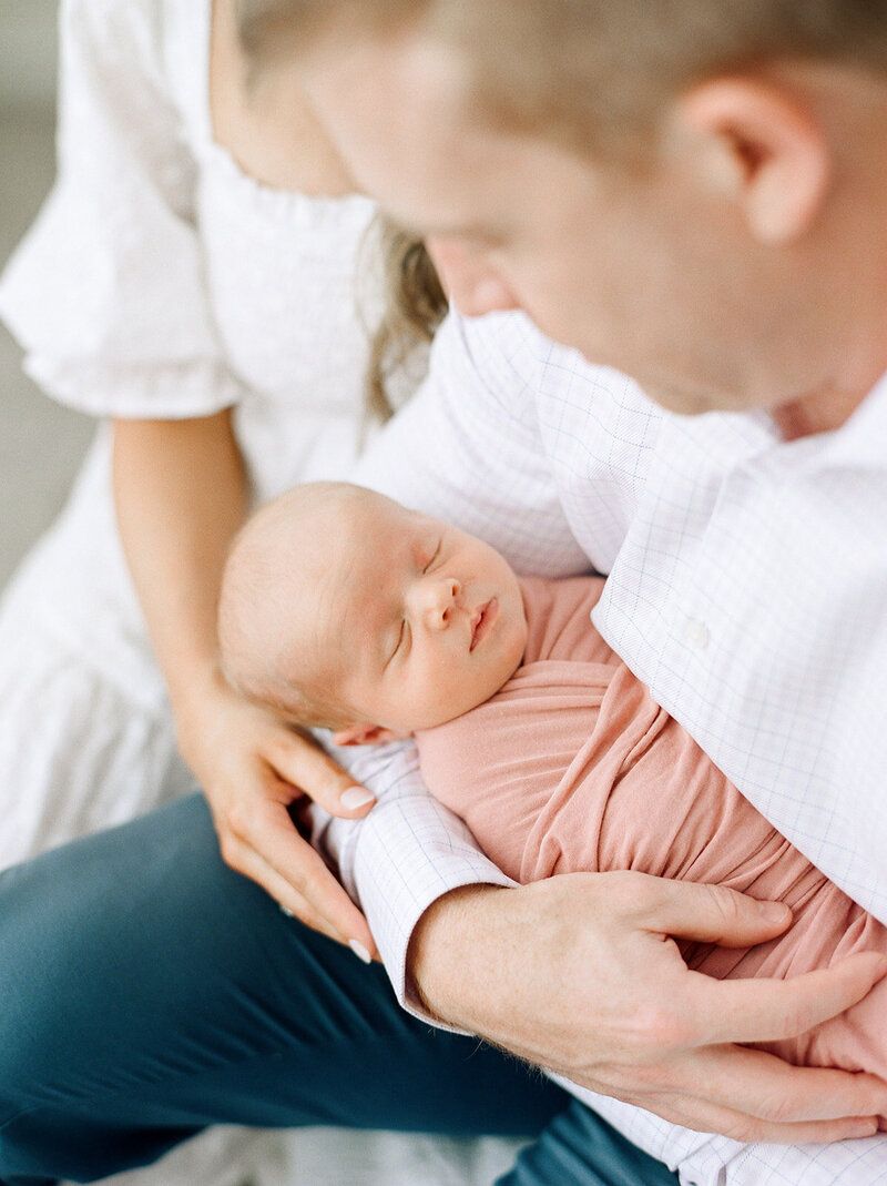 Tender moment with sleeping newborn cradled by parents in white.