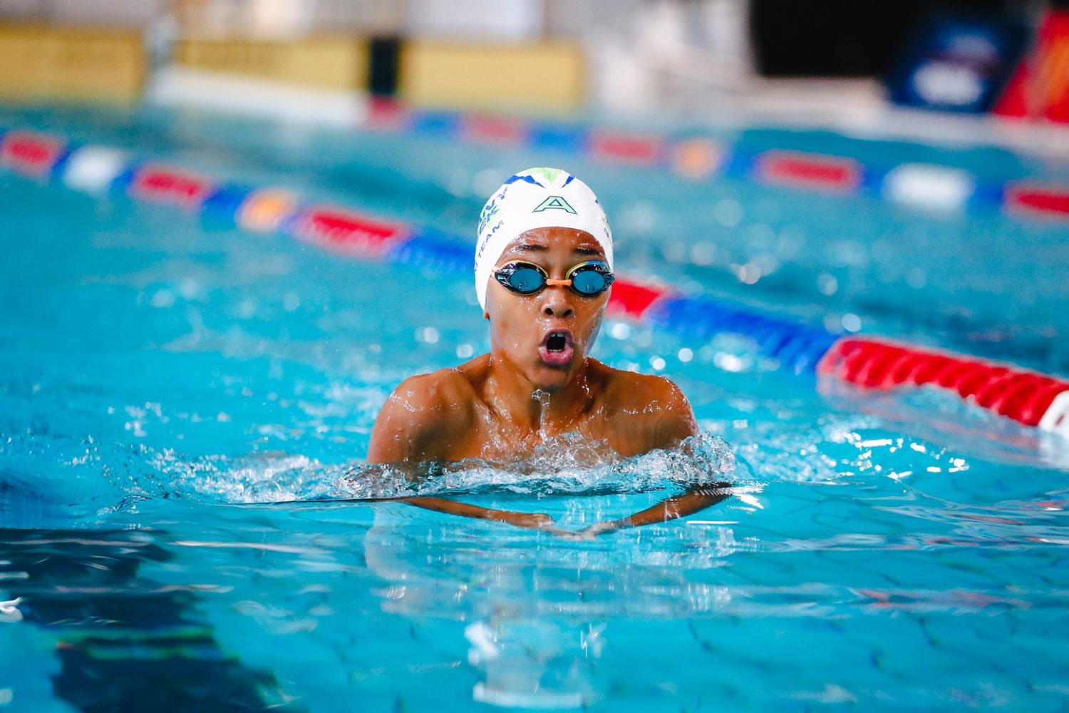 Competitive swimmer performs breaststroke during swim meet with red lane lines visible.