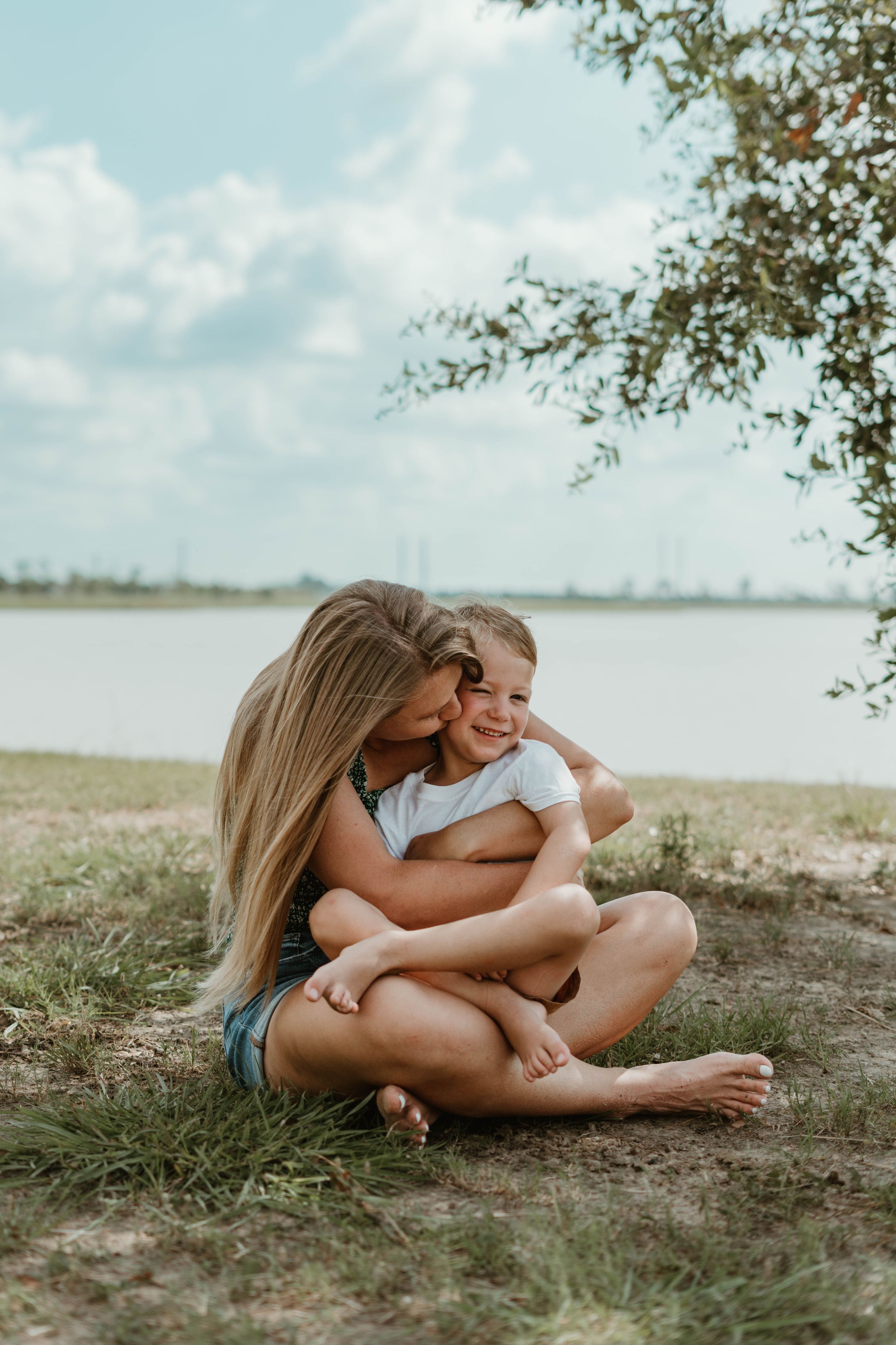 Sweet candid moment shared beside tranquil lake under cloudy summer sky.