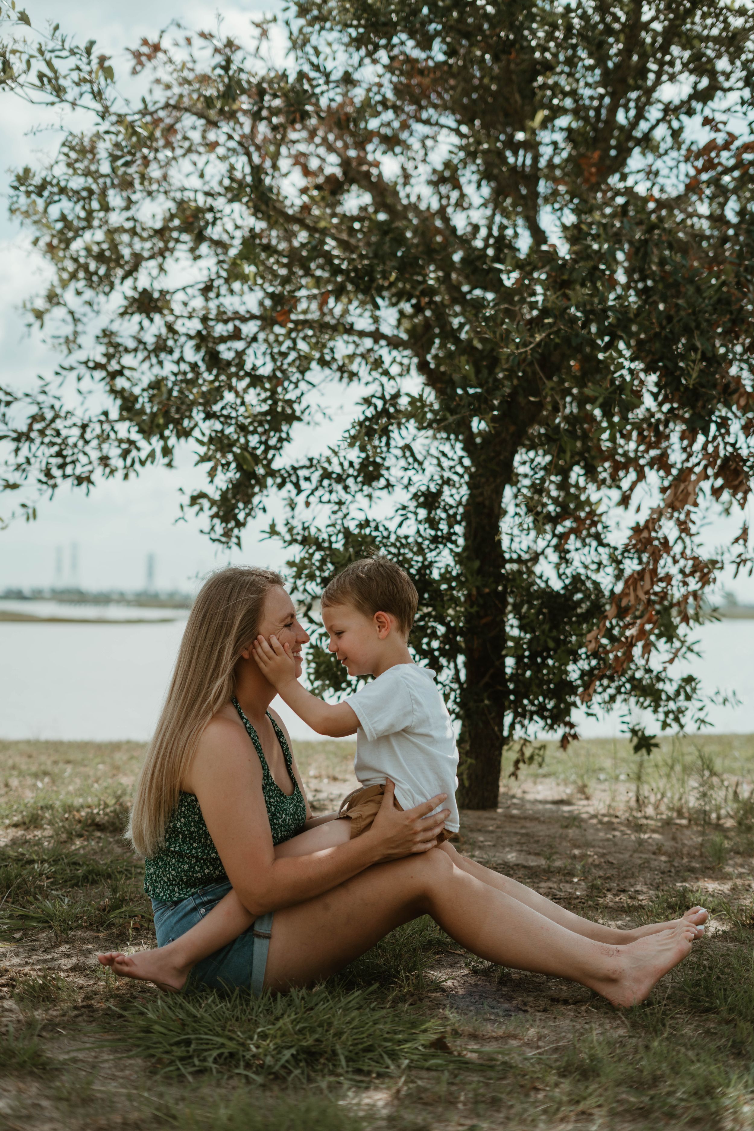 A tender moment captured under a tree by a lake on a summer afternoon.