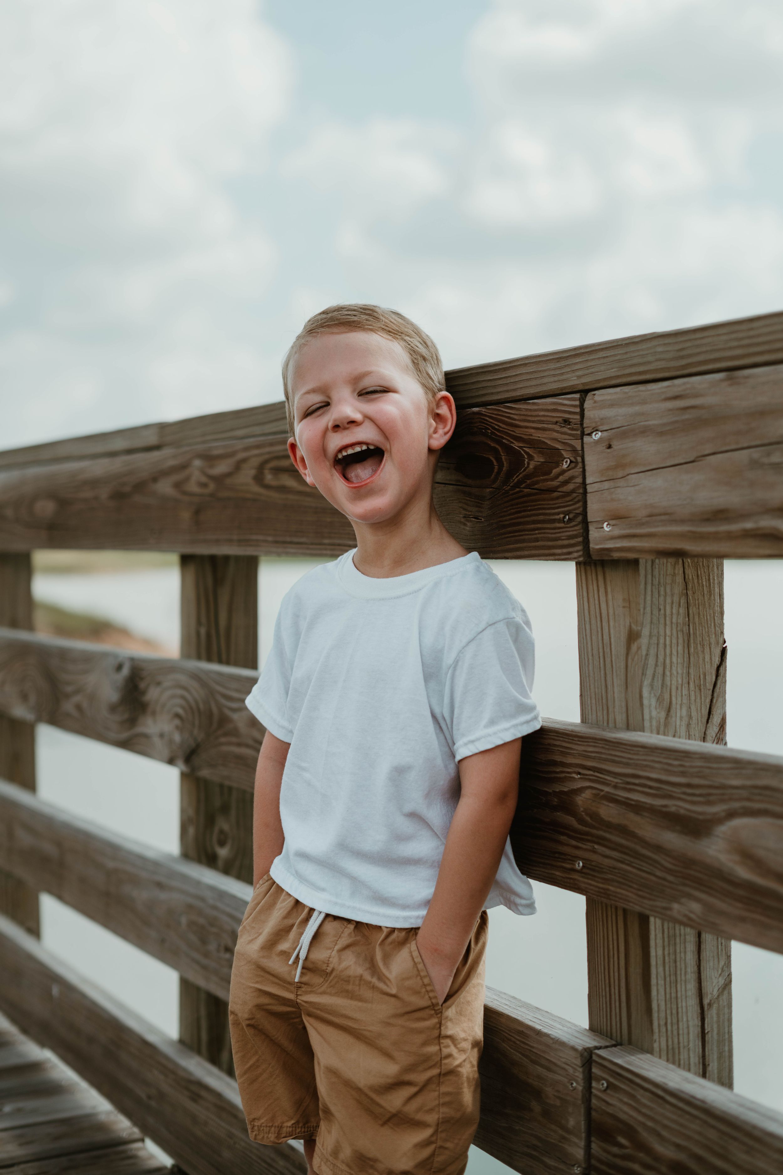 A joyful child laughing while standing against a wooden railing on a boardwalk.