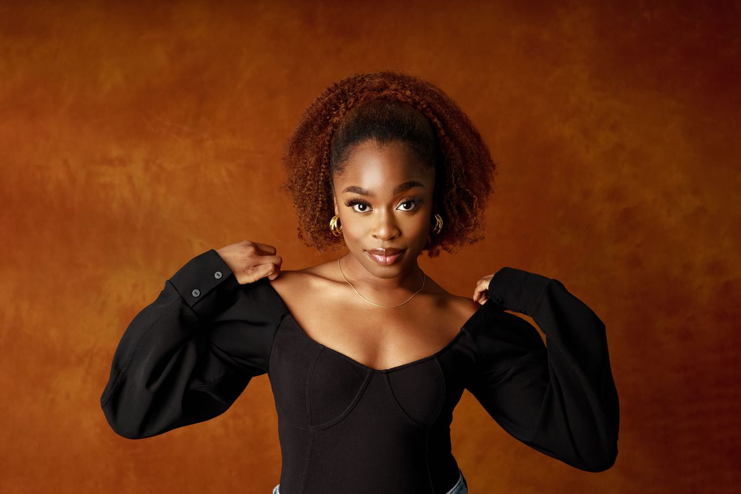 Studio portrait against brown background featuring dramatic black puff-sleeve top.