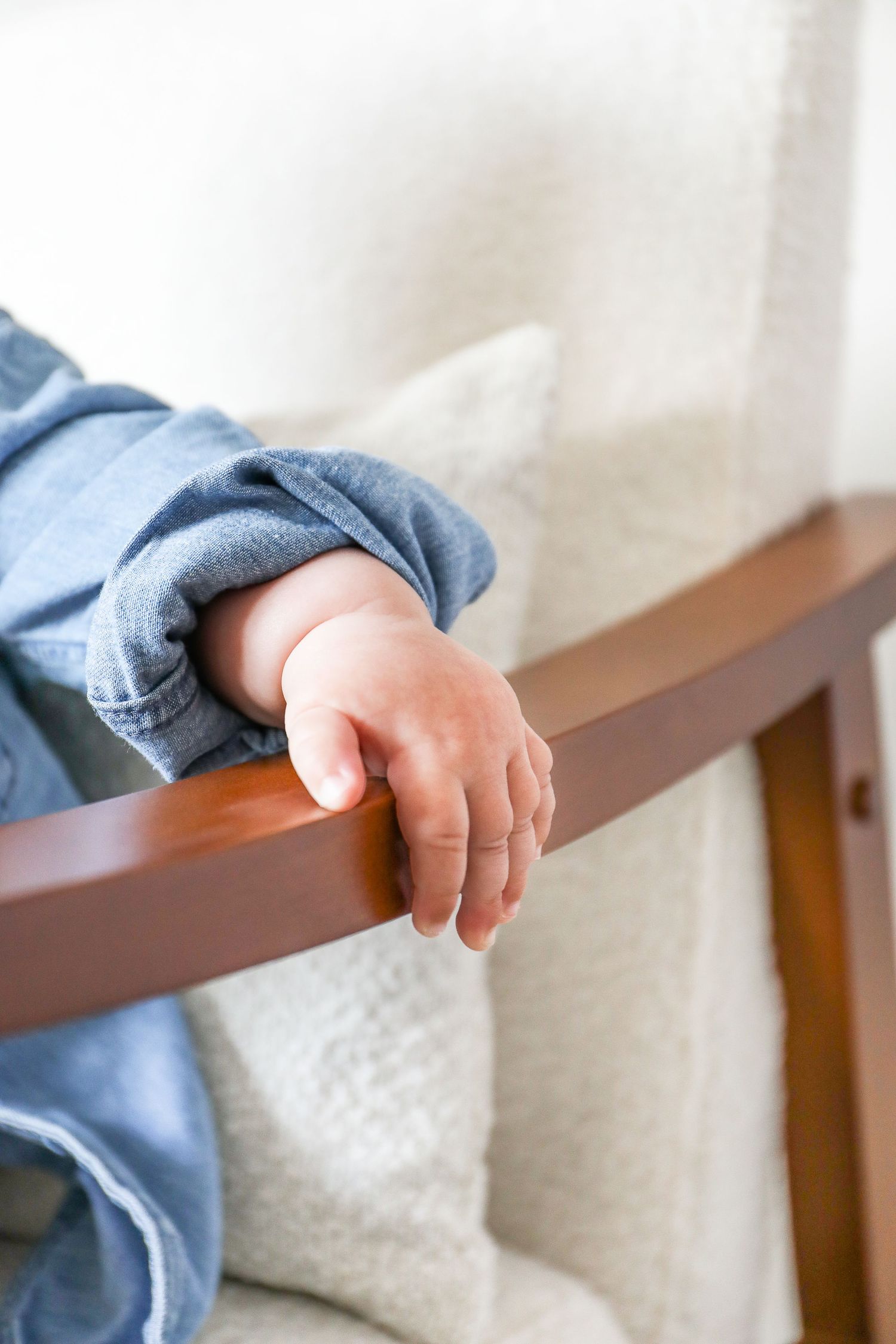 A tiny baby hand rests on a wooden chair wearing light blue sleeves, during Sitter photoshoot based in Nottingham