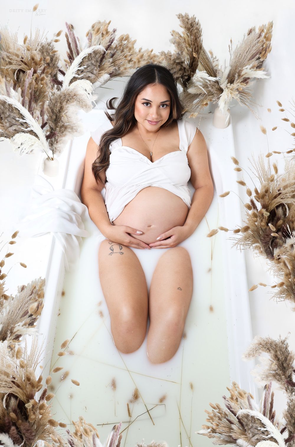 Artistic maternity photo with white dress and dried pampas grass decorations.