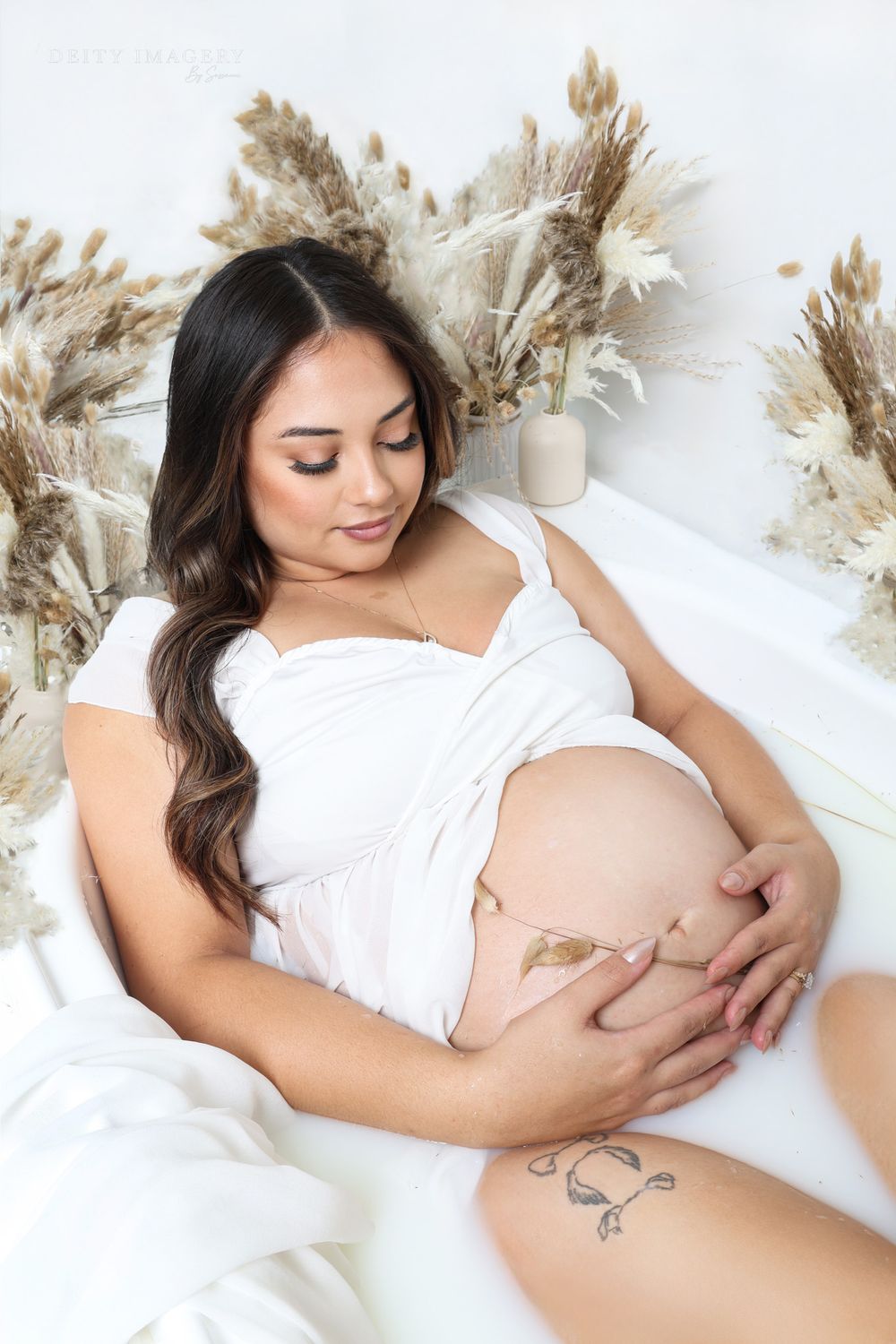 Intimate maternity session with white fabric and pampas grass details on light background.
