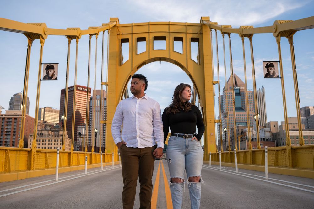Couple standing on Pittsburgh's iconic Roberto Clemente Bridge with downtown skyline in background.