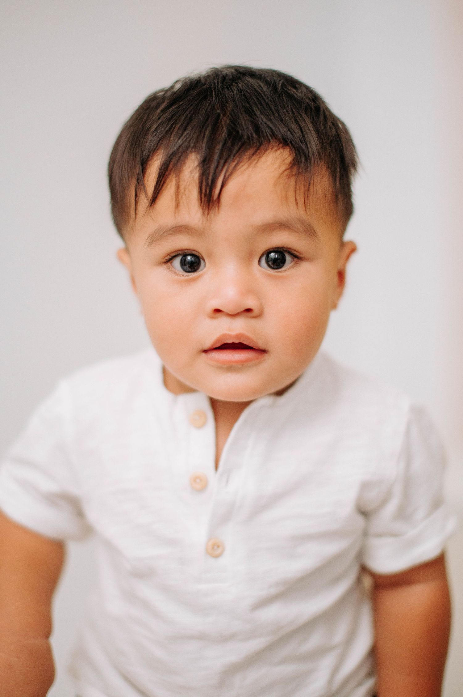 Child wearing a white short-sleeved henley shirt poses against neutral background in studio portrait.