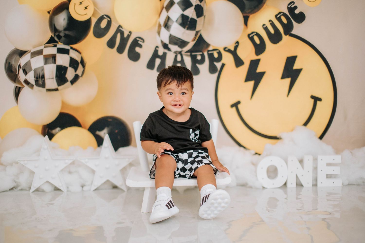 Birthday party setup with black and gold balloons featuring smiley face designs and 'ONE HAPPY DUDE' text decoration.