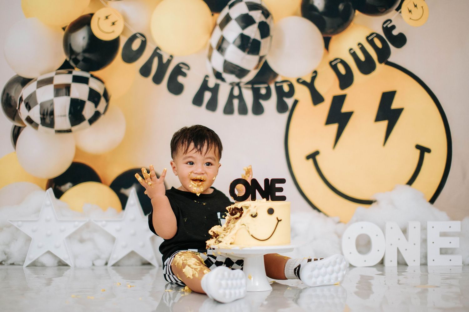 First birthday celebration setup with black and yellow decor featuring smiley face balloons and lightning bolt designs.