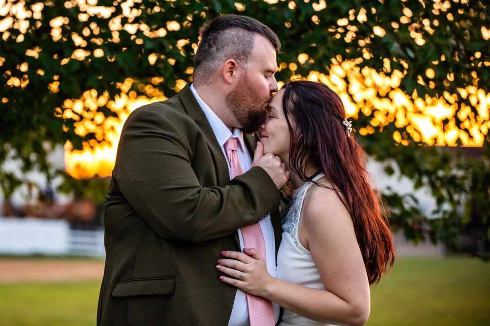A romantic couple shares a tender moment at sunset in a park setting with golden bokeh lighting in the background.