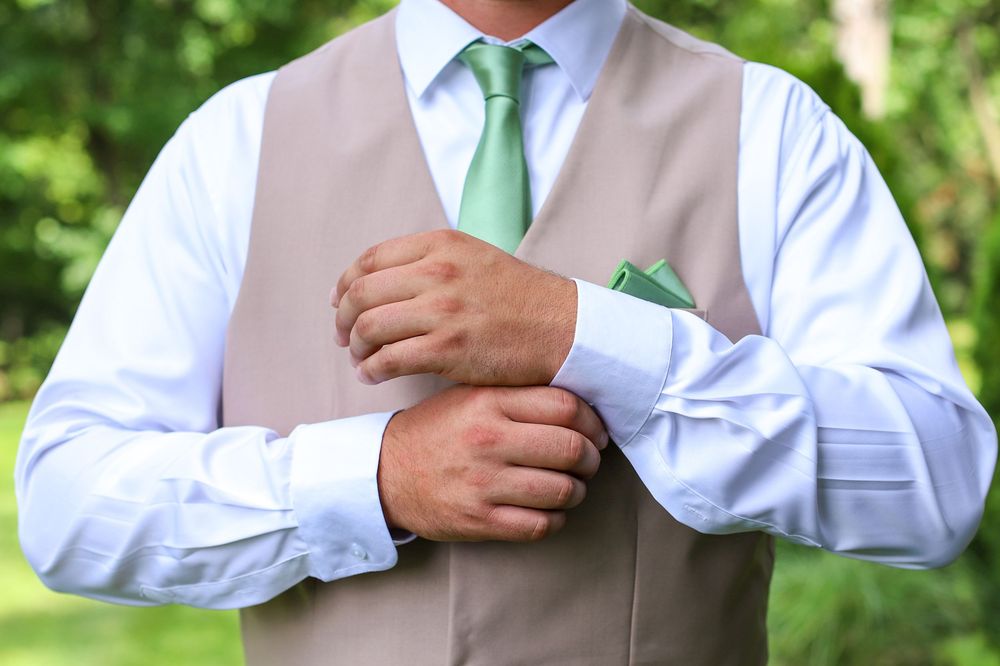 A series of photos showing someone adjusting a light green tie with a white shirt and beige vest.