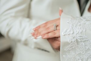 Close-up of a bride wearing a diamond wedding ring set on her hand, with white lace wedding dress detail.