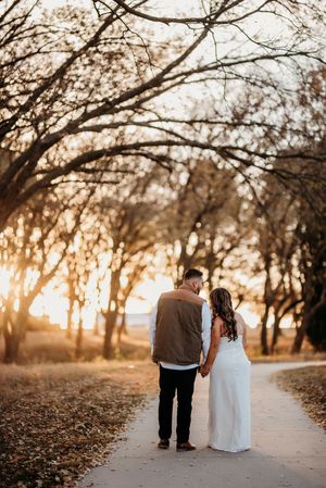 A couple strolls together on a sunset-lit path surrounded by autumn trees.
