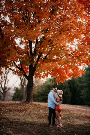 A couple embraces under a stunning maple tree with bright red fall foliage.
