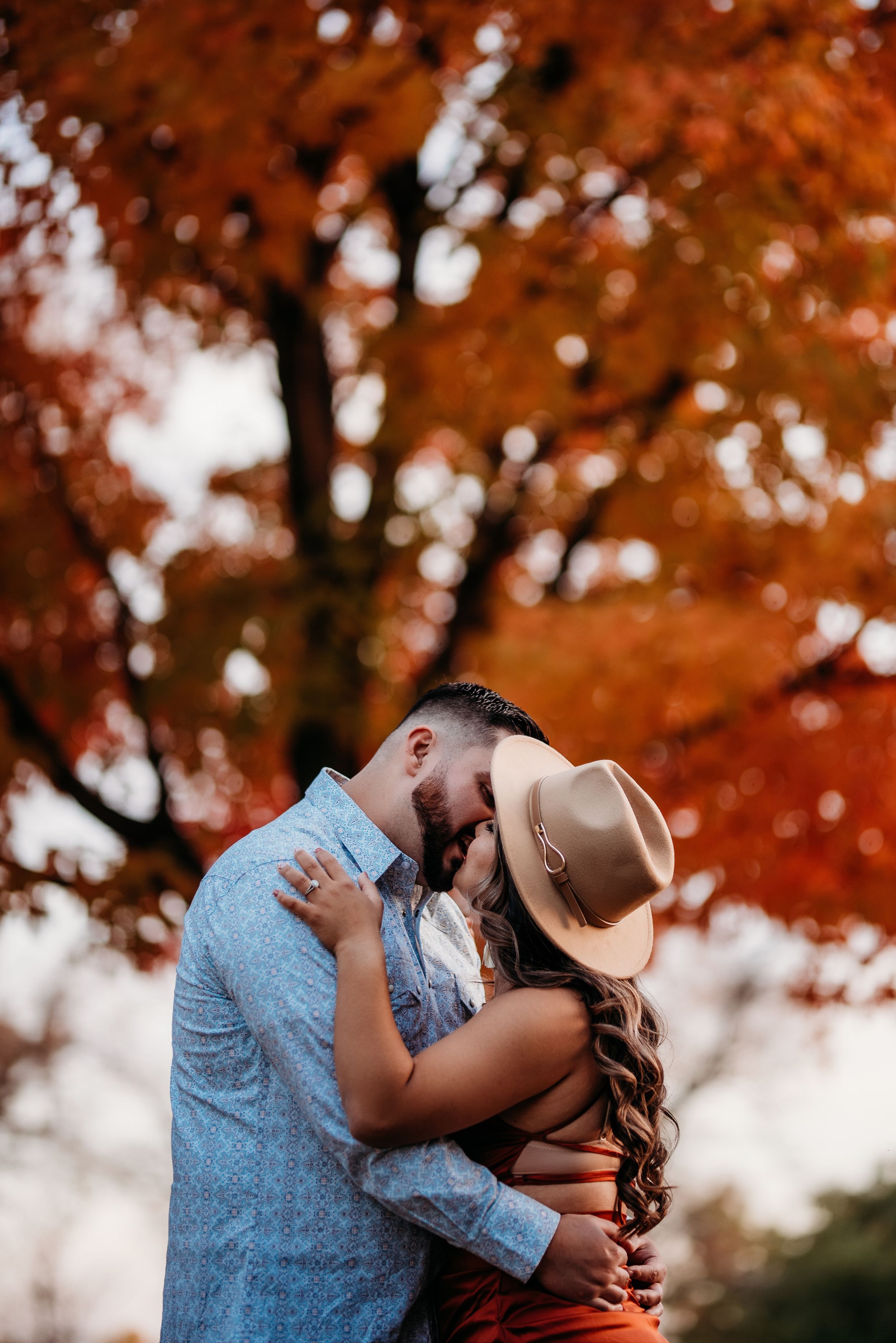 A romantic moment captured under vibrant orange autumn trees during an engagement session.