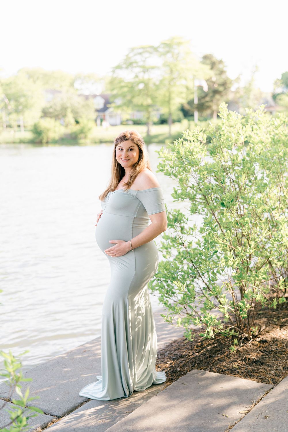 Elegant portrait of expecting mother by green trees overlooking the lake at Divine Park, Spring Lake.