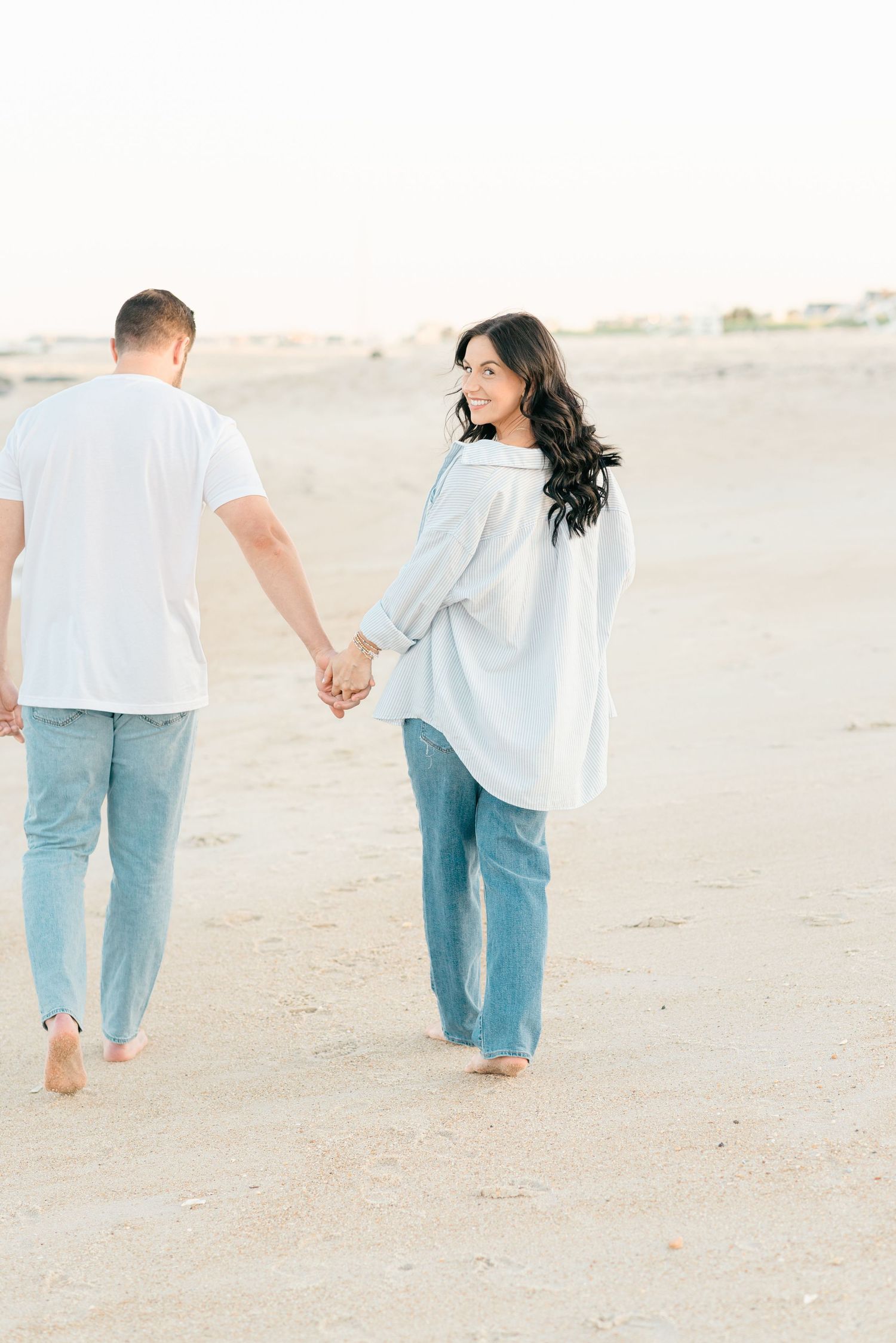 Pregnant woman with dark brown hair holds her husbands hair while looking back at Lauren Marie Photography.