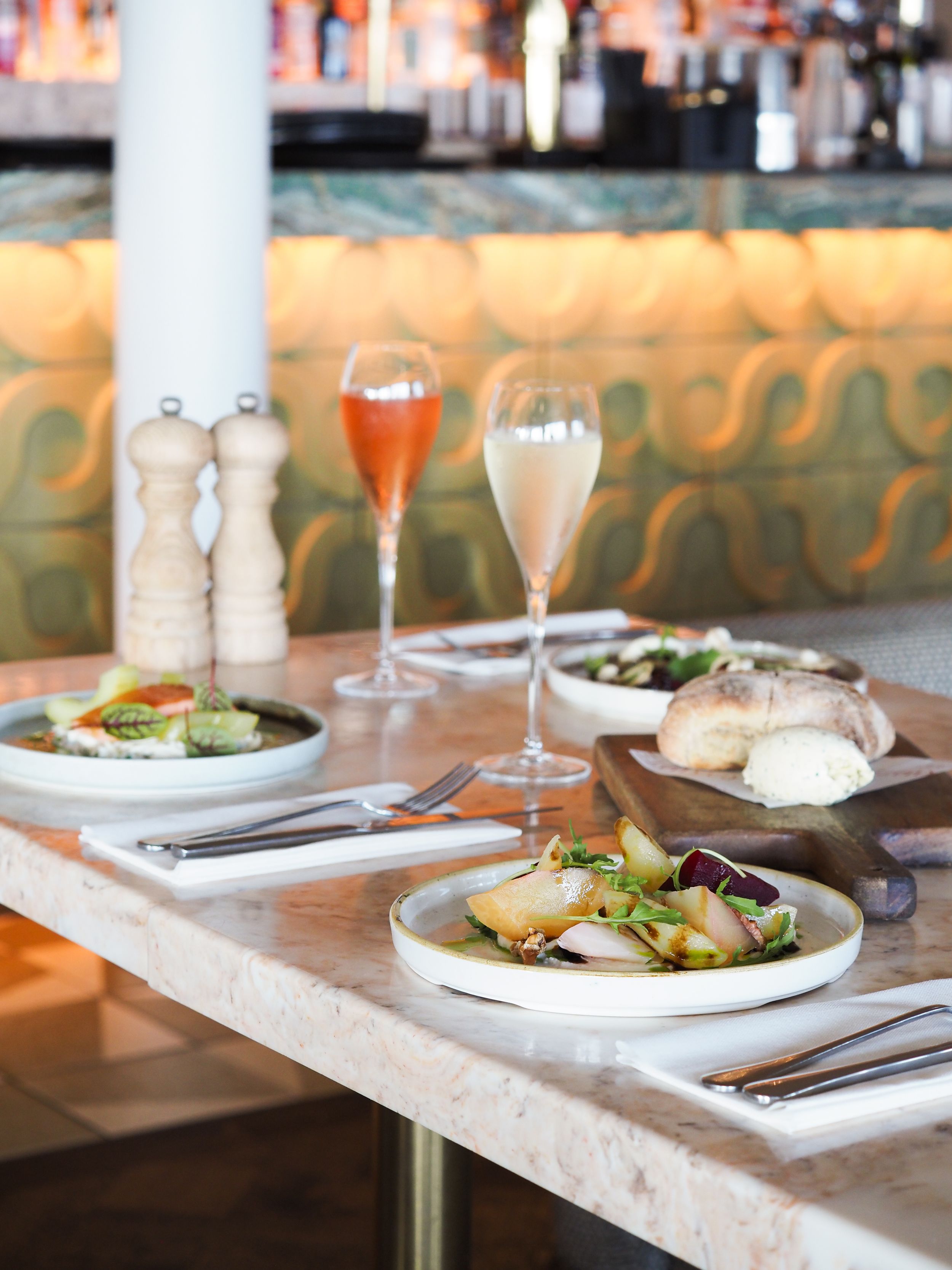 Elegant restaurant table setting with champagne flutes, fresh salads, bread, and pepper mills on a marble surface.