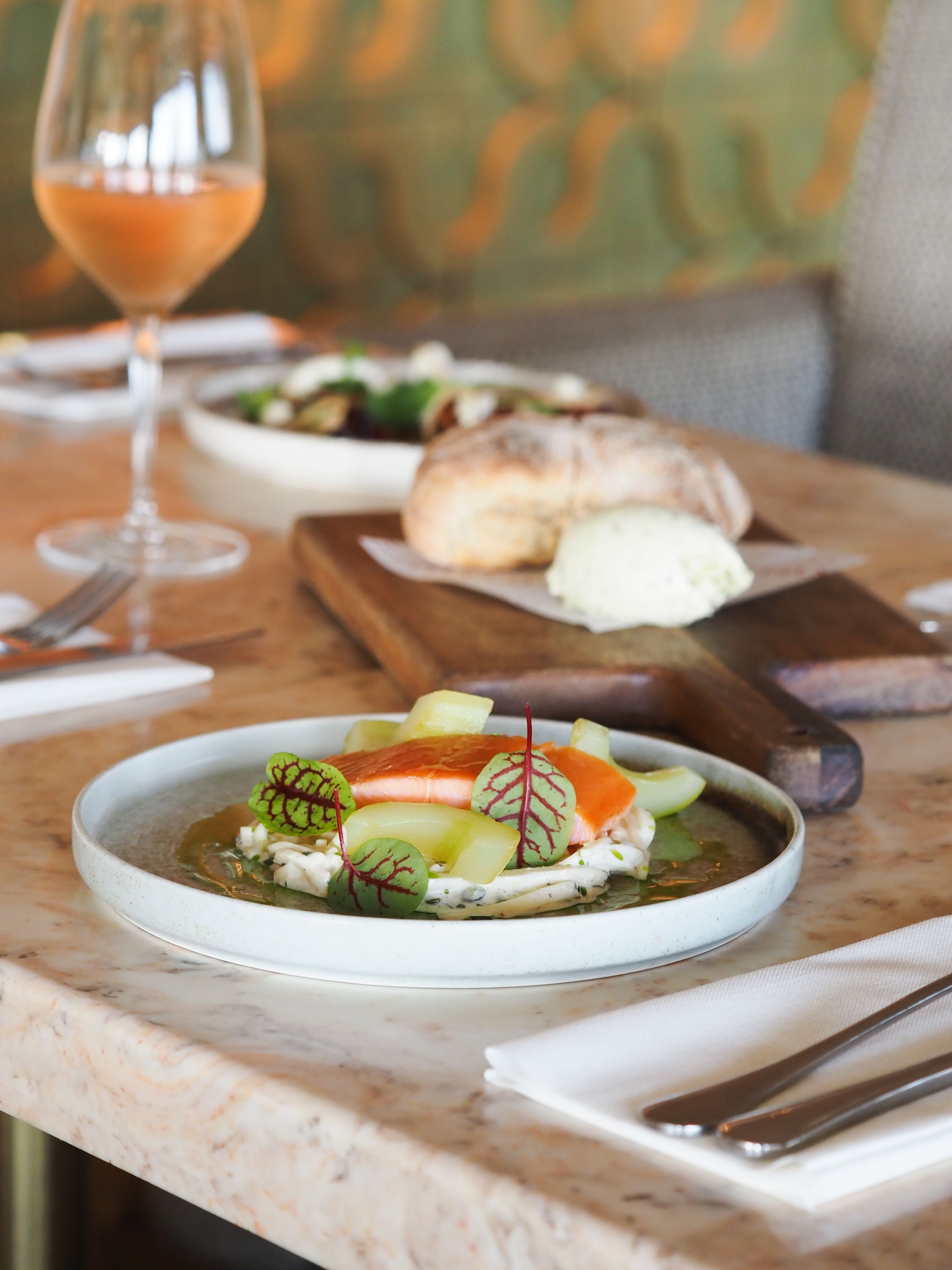 Elegant plated dish with colorful vegetables and garnish on marble table with wine glass at upscale restaurant.