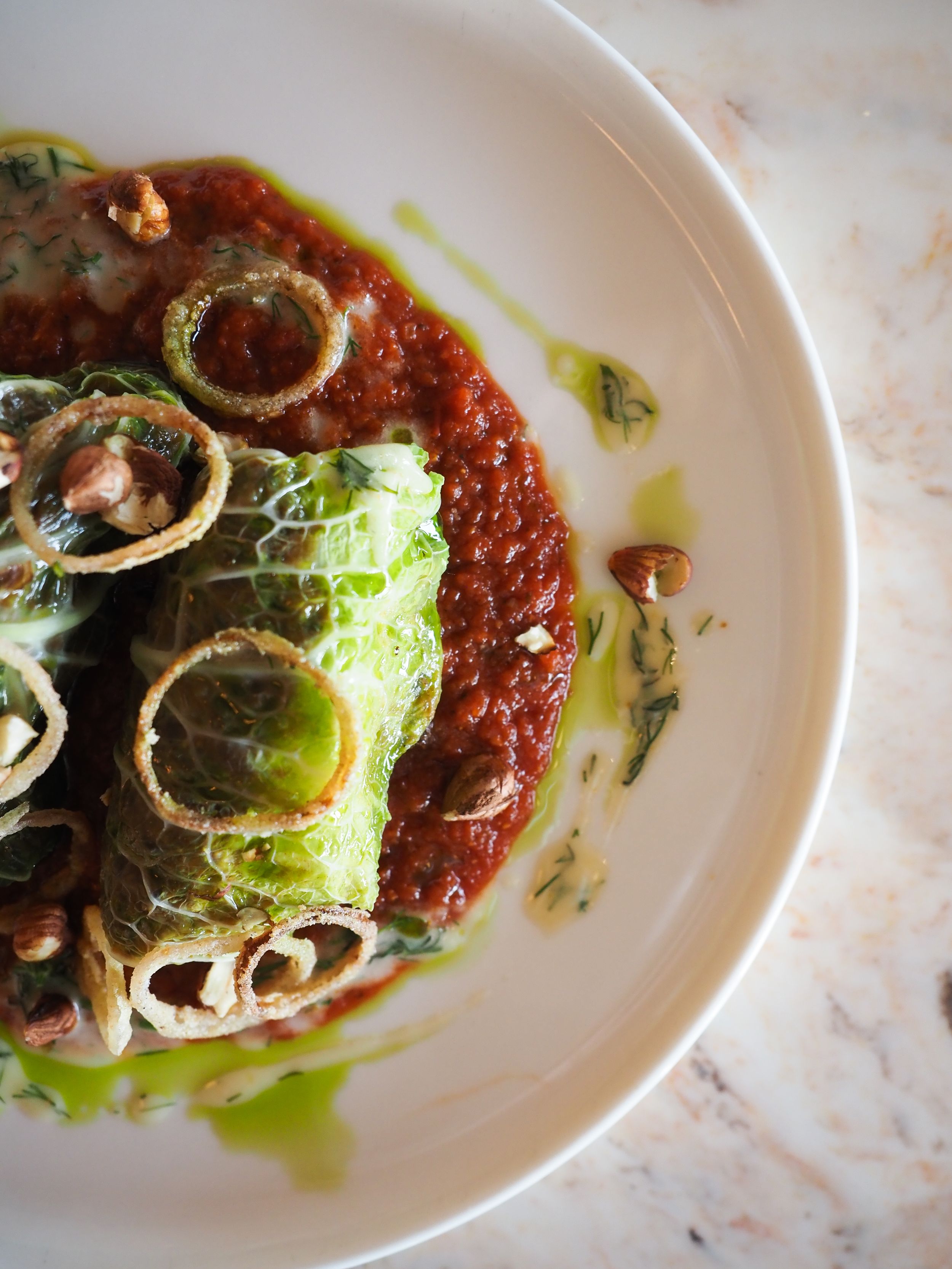 Elegant cabbage rolls with tomato sauce, walnuts, and herb oil drizzle in a white ceramic bowl.