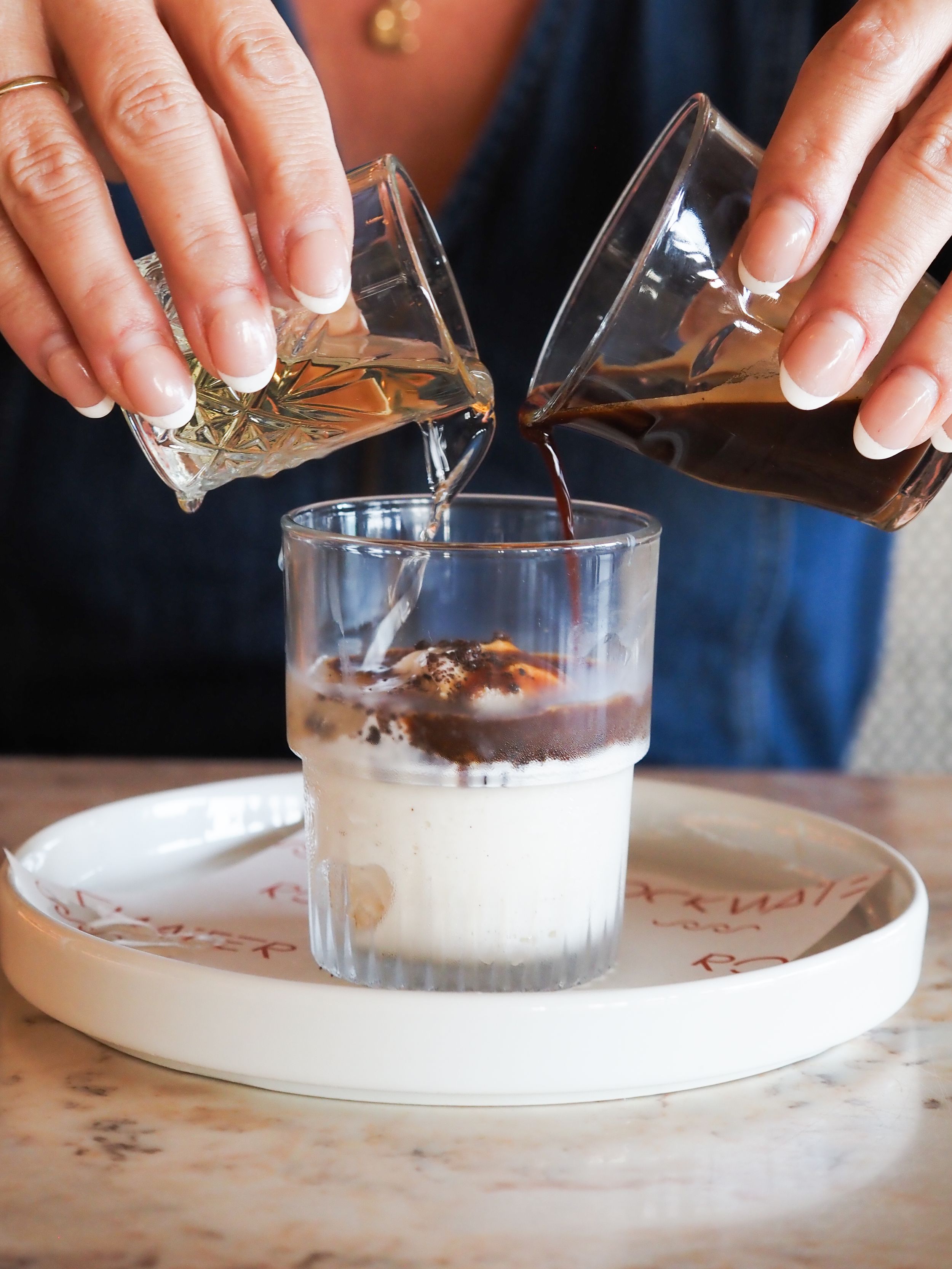Person pouring espresso shots over milk in a glass on a marble tray, making an iced latte.