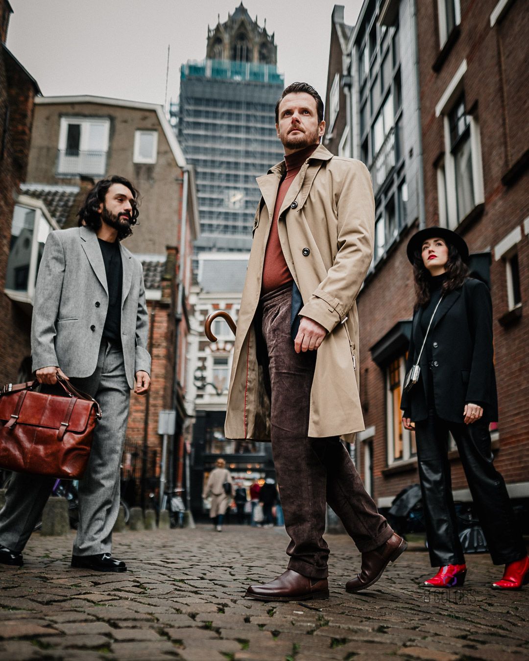 Three people standing on a cobblestone street in an urban area with tall buildings and modern architecture in background.