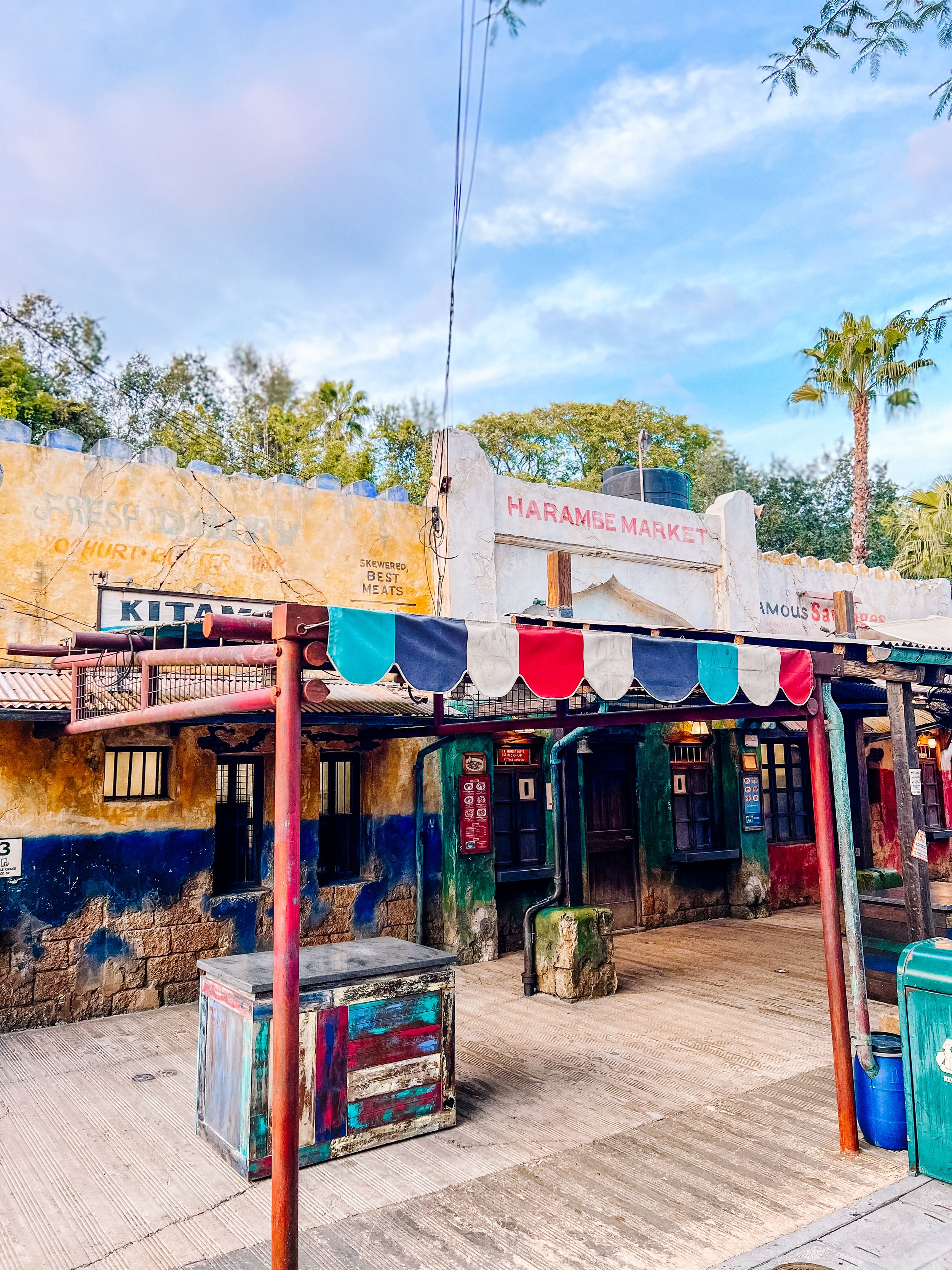 Outdoor market stalls with colorful awnings and clothing displays line a pathway in a sunny tourist shopping area.