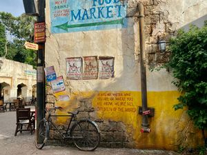 A vintage bicycle leans against a weathered wall with yellow and beige paint beneath a market sign in an old town setting.