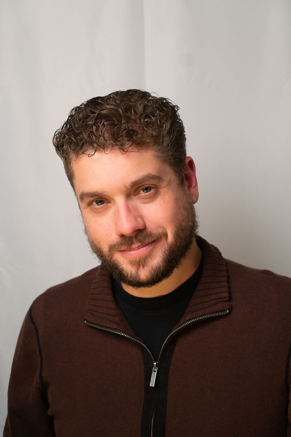 Person wearing brown zip-up jacket and black shirt smiling at camera.