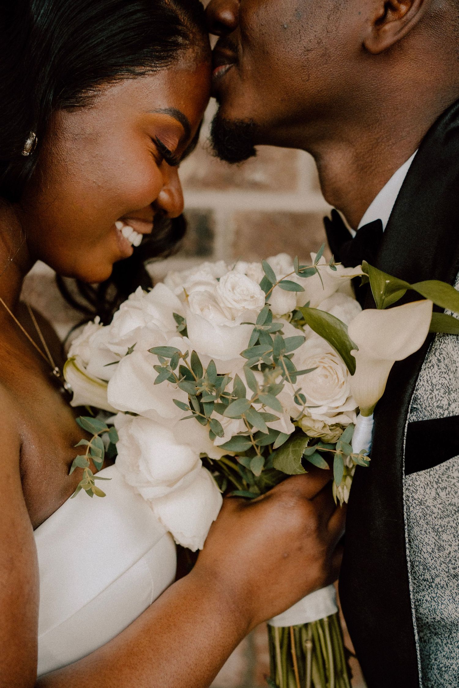 A beautiful bridal bouquet of white roses and eucalyptus sits between an intimate wedding couple moment.