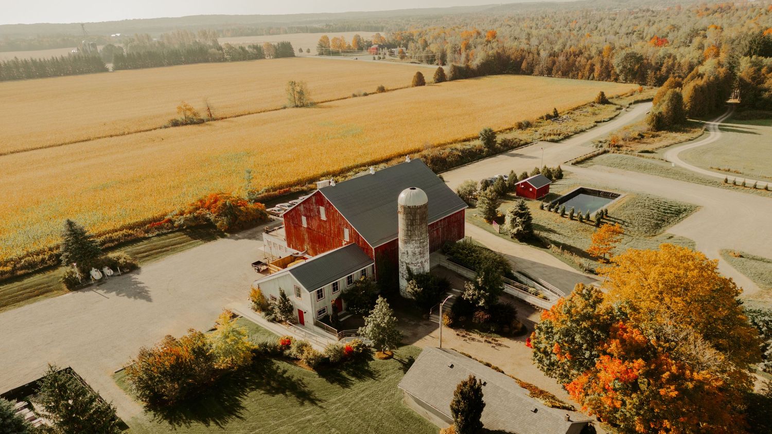 Aerial view of a rustic red barn and silo surrounded by autumn farmland.