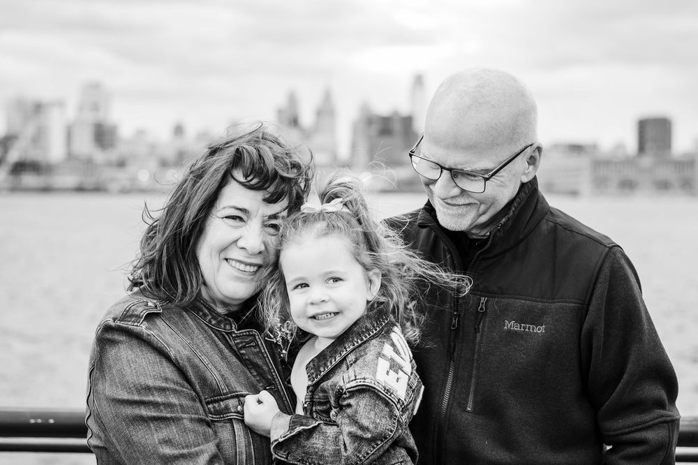 A young family shares an intimate moment together outdoors with the city skyline in the background.