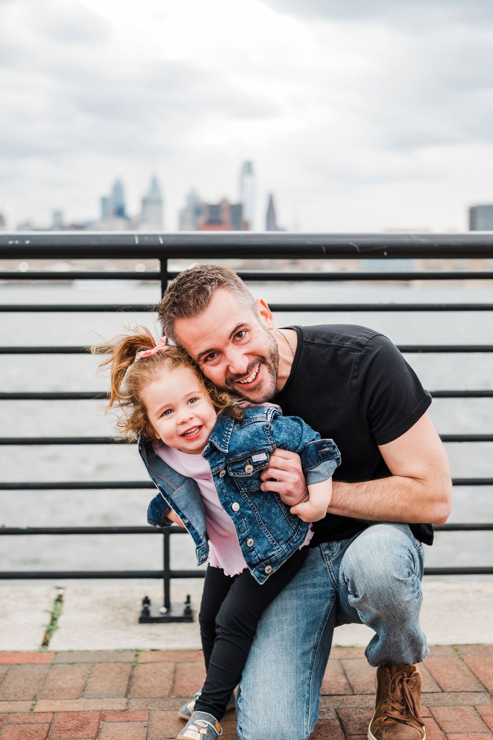 A parent and child share a happy moment together on a brick patio with the Philadelphia city skyline in the background.