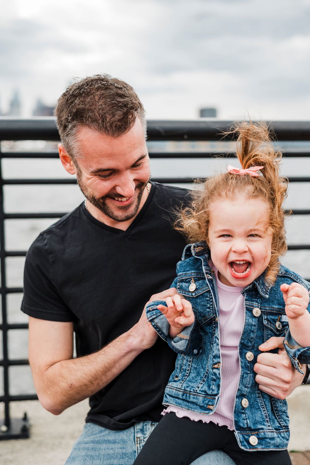 A joyful moment shared between two people laughing together against a city backdrop on a cloudy day.