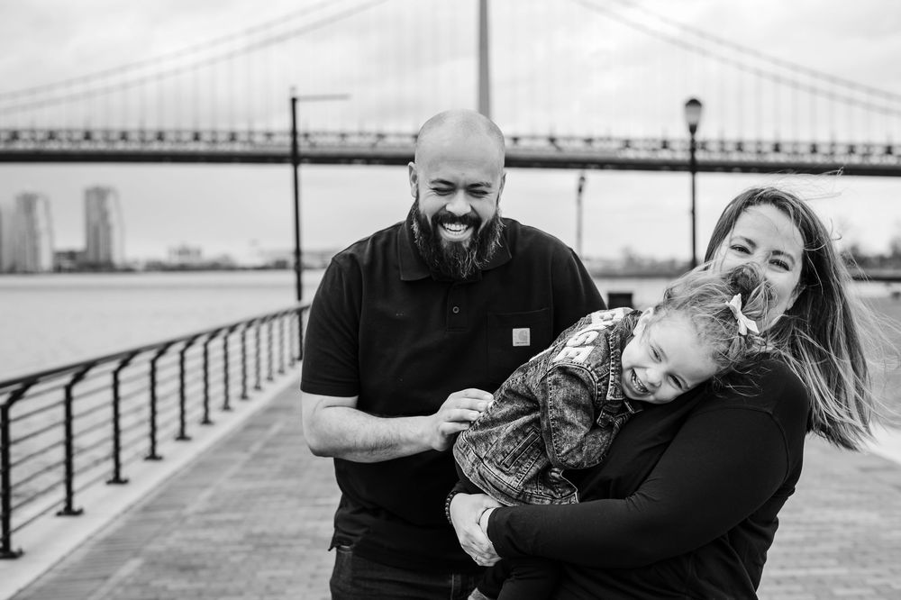 A family shares a joyful moment together along the waterfront with a bridge visible in the background.