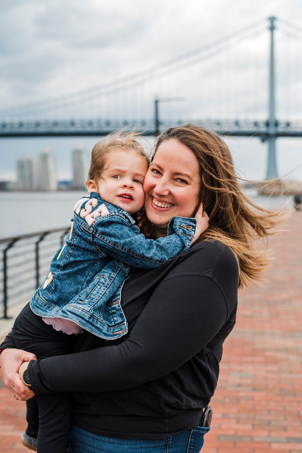 A joyful embrace between parent and child near a waterfront with a bridge in the background.