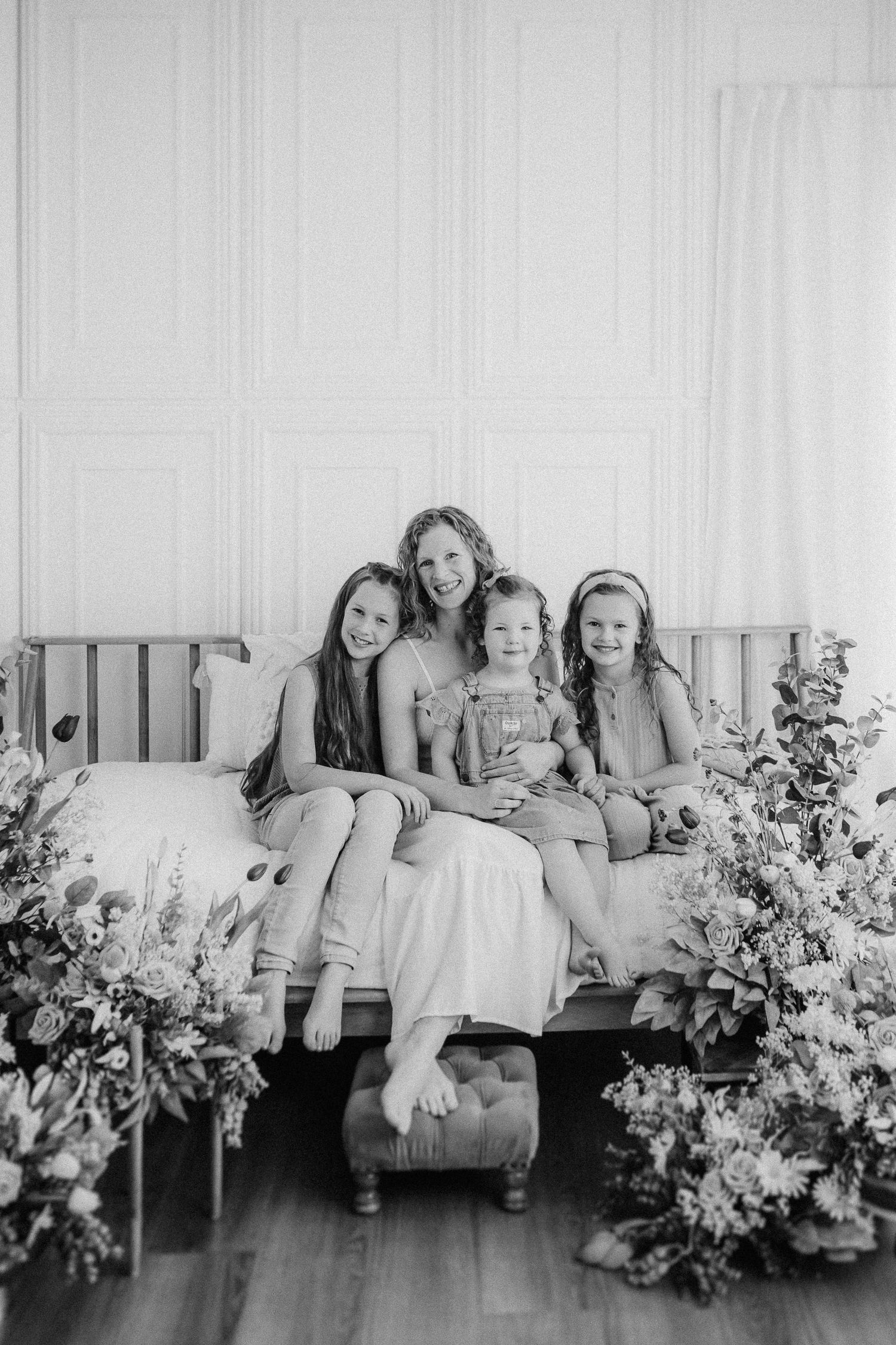 Black and white portrait showing a group seated on a couch with decorative floral arrangements on both sides.