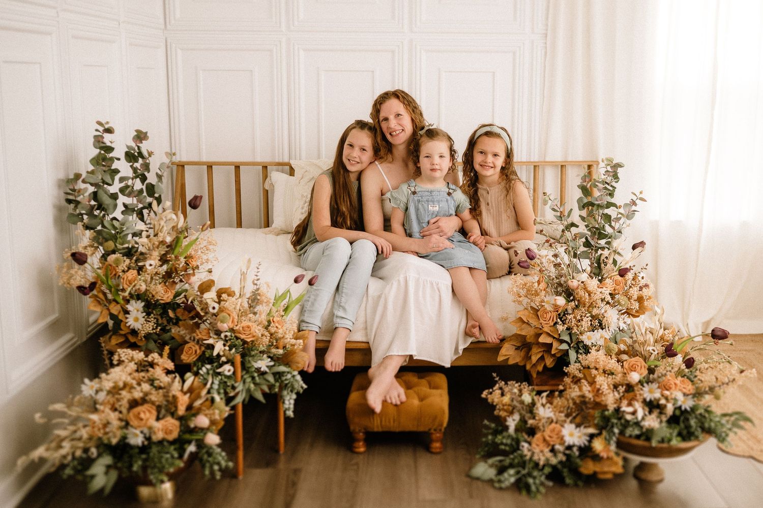 A bright rustic photoshoot setup with floral arrangements placed around a wooden bench with sheer drapes in the background.
