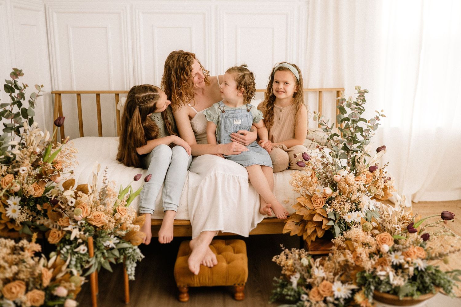 A group sits on a bed surrounded by lush peach and cream floral arrangements in a bright, airy room.